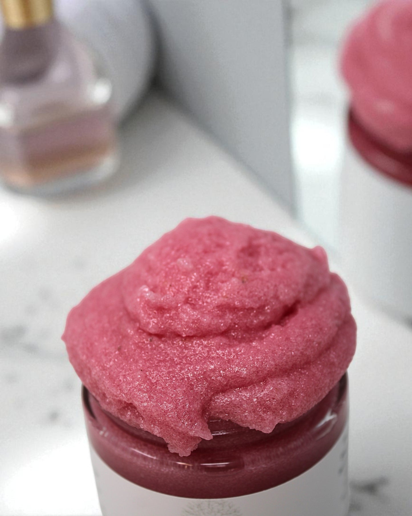 Pink scrub in a jar on a marble surface with a blurred background