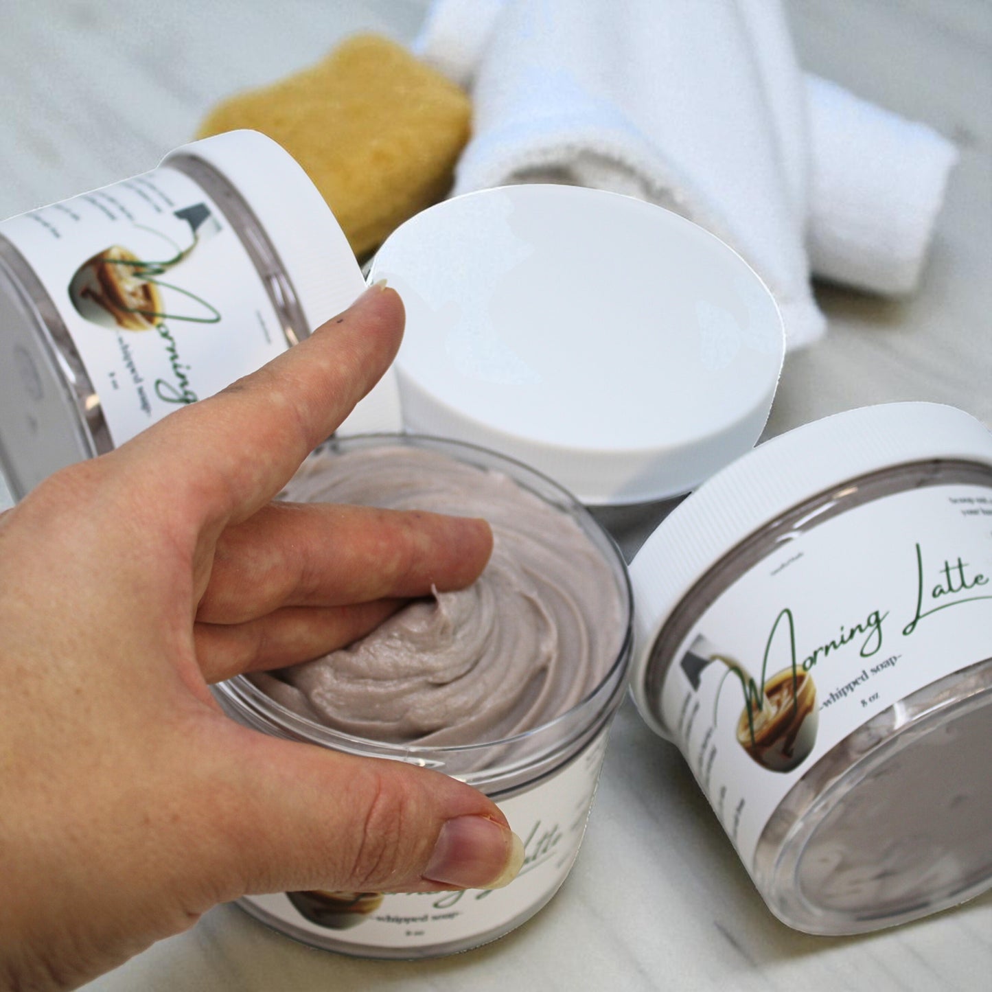 Hand holding a jar of 'Morning Latte' whipped cream with another jar and a towel in the background.