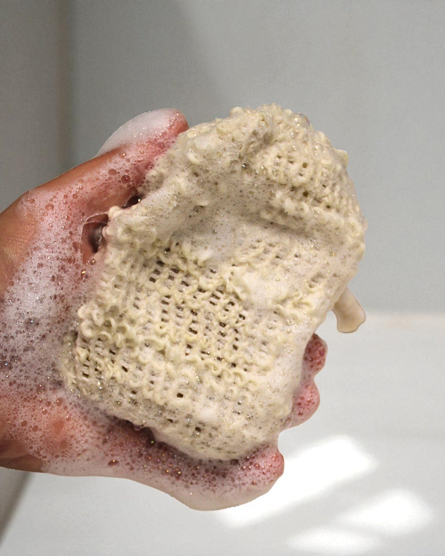 Hand holding a lathered bar of soap with a textured surface.